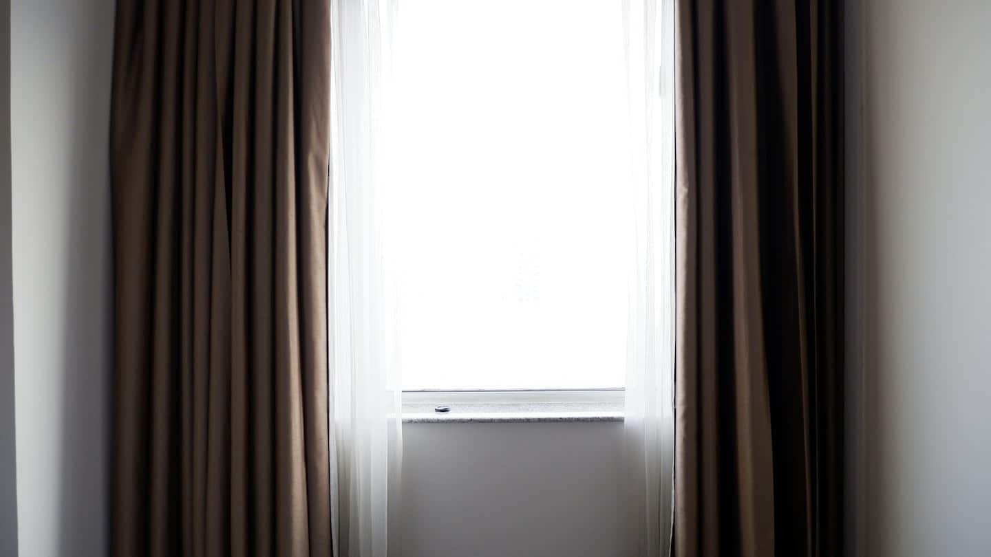 La luce del sole filtra da una finestra incorniciata da tende bianche e marroni.