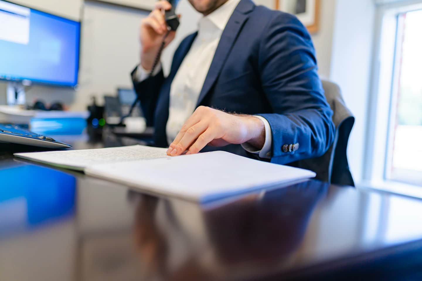 Un uomo d'affari in giacca e cravatta parla al telefono fisso alla sua scrivania.