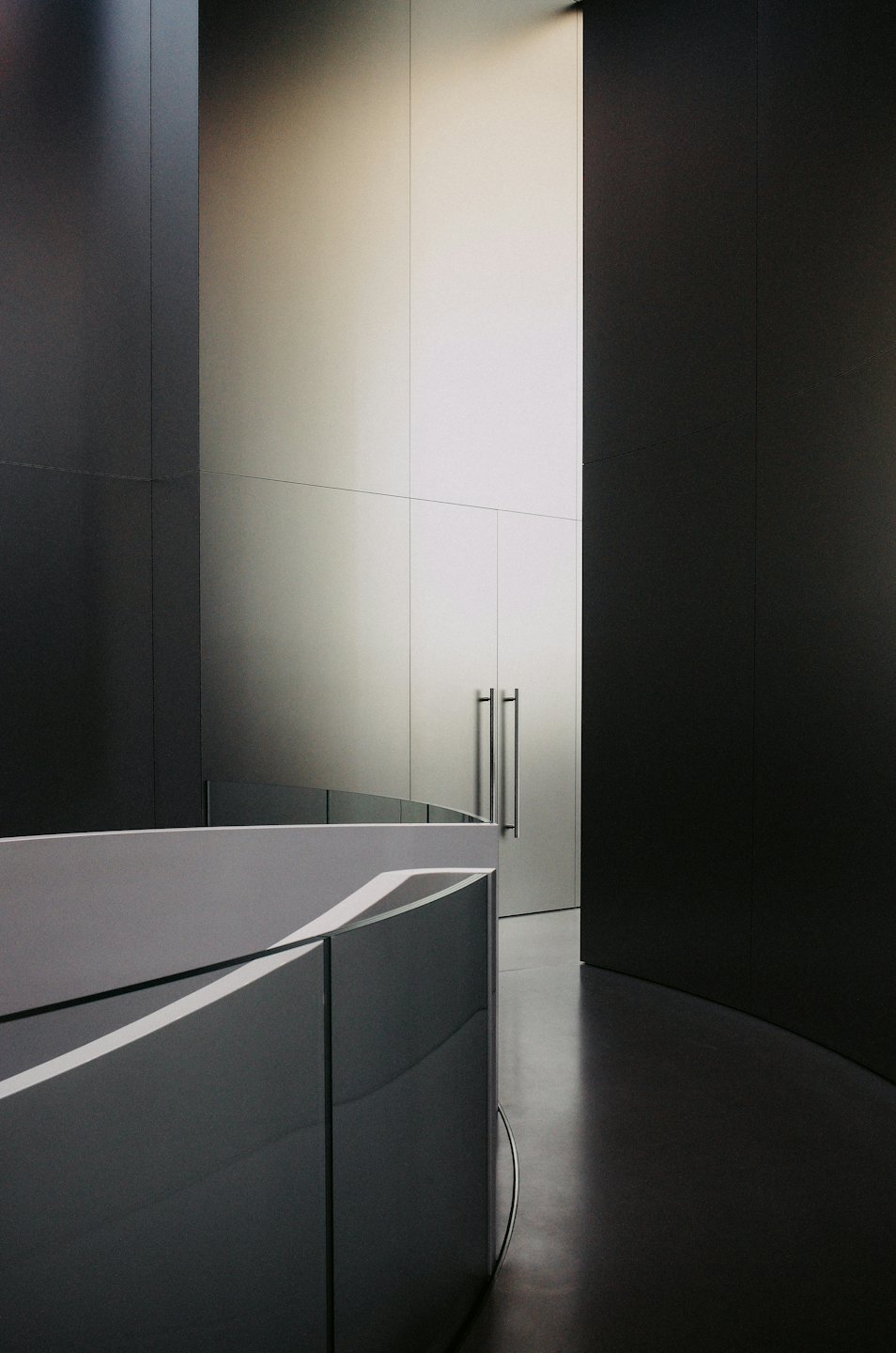 Una parete curva conduce a una parete illuminata con maniglie delle porte.